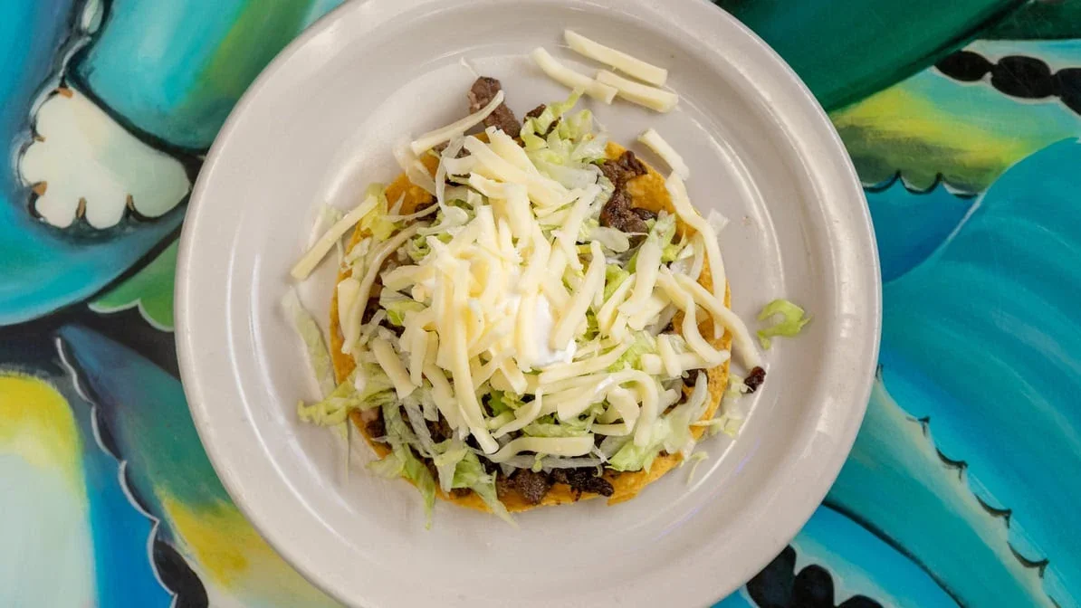 Tostada - Crispy tostada topped with beans, meat, lettuce, and cheese